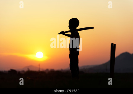 Silhouette of young Indian boy playing cricket against a sunset background Stock Photo