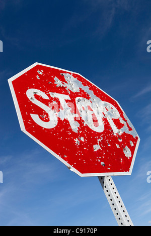 A stop sign on a highway in the American west that is riddled with bullet holes from people shooting it and using it as a target Stock Photo