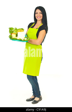 Full length of smiling cheesemaker woman with green apron holding different cheese on plateau in a supermarket isolated on white Stock Photo