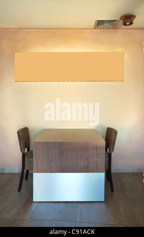 Table and chairs in a restaurant with empty frame on the wall. Stock Photo