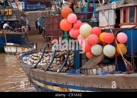 there are trawler boats with colourful floats docked in muddy waters in Skala du Porte with fishermen preparing nets. Stock Photo