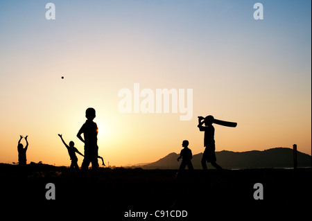 Silhouette of young Indian boys playing cricket against a sunset background Stock Photo