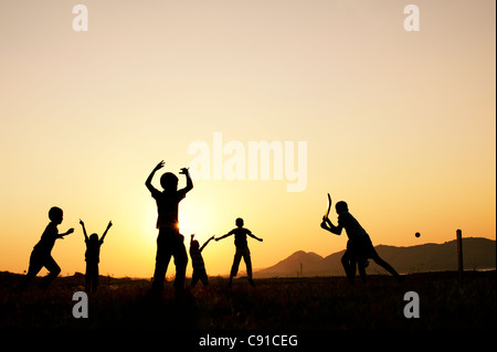 Silhouette of young Indian boys playing cricket against a sunset background Stock Photo