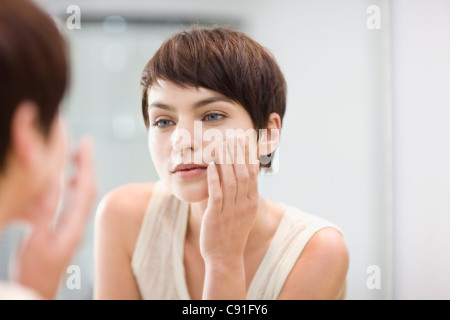 Woman applying moisturizer in mirror Stock Photo