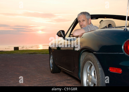 Man sitting in convertible on coastline Stock Photo