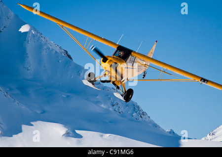 Yellow Piper Super Cub with wheel skis preparing to land on a glacier in the Neacola Mountains, Winter in Southcentral Alaska Stock Photo