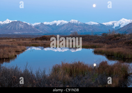 A full moon reflects on the surface of a small pond after sunset in Denali National Park & Preserve, Interior Alaska, Autumn Stock Photo