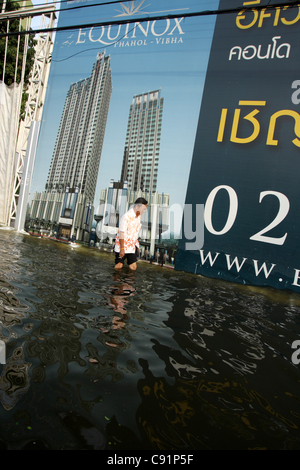 A man wading through floodwaters near advertisment screen on November 8, 2011 Bangkok , Thailand. Over seven major industrial parks in Bangkok and thousands of factories have been closed .Thailand is experiencing the worst flooding in over 50 years . Stock Photo