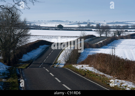 Windy bumpy road cutting through the snow fields of the countryside in winter,  England Stock Photo