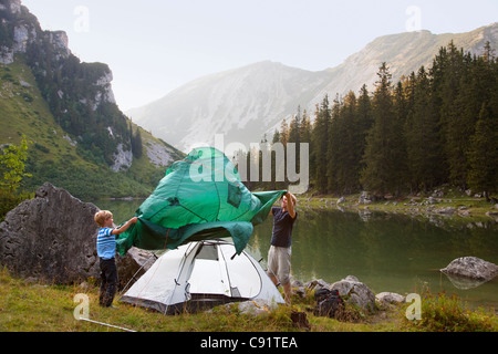 Father and son pitching a tent by lake Stock Photo