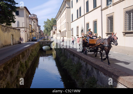Tourists take horse drawn carriage rides on the Via Del Fosso in Lucca beside the waer course. Stock Photo