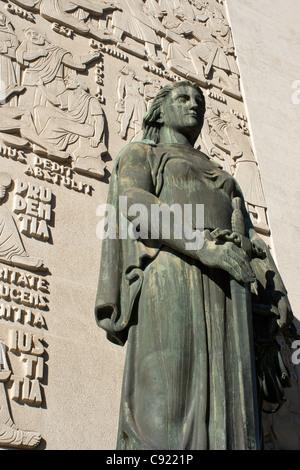 There is a bronze sculpture of a woman with sword against a wall of stone carving on the Palacio de Justica court on Campo dos Stock Photo