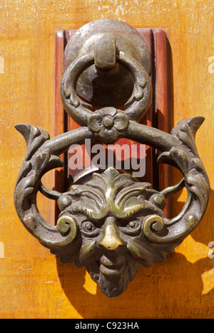 An ornate door knocker in the shape of a human face, with a wicked expression, on a door in the town of Mosta. Stock Photo