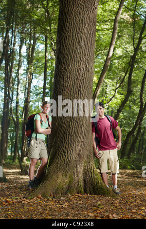 young man and woman during hiking excursion, posing near large tree and smiling. Vertical shape, front view, full length Stock Photo
