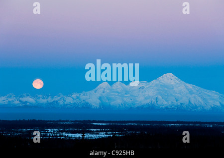 A full moon sets over Mt. Iliamna as seen from Nikolaevsk on the Kenai Peninsula, Southcentral Alaska, Winter Stock Photo