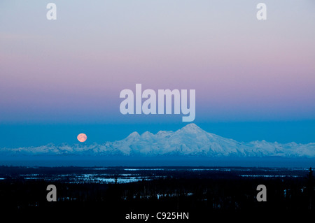 A full moon sets over Mt. Iliamna as seen from Nikolaevsk on the Kenai Peninsula, Southcentral Alaska, Winter Stock Photo