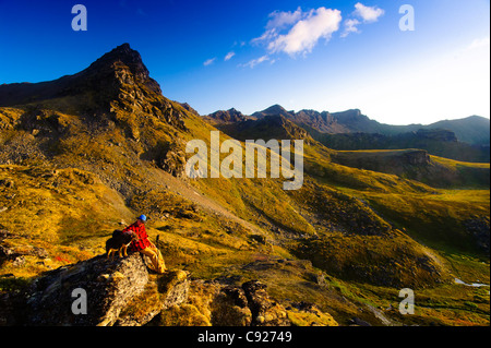 A man sitting on a rock while hiking with his dog near Hatcher Pass in the Talkeetna Mountains, Alaska Stock Photo