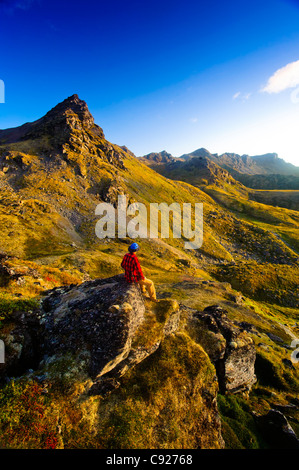 A man sitting on a rock while hiking near Hatcher Pass in the Talkeetna Mountains with Bald Ridge in the background, Alaska Stock Photo