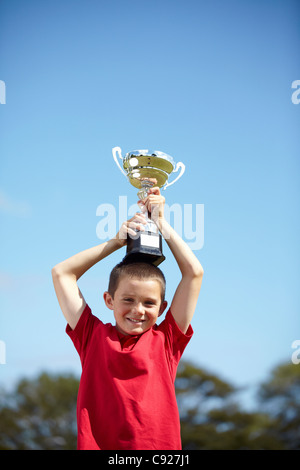 Boy cheering with trophy outdoors Stock Photo