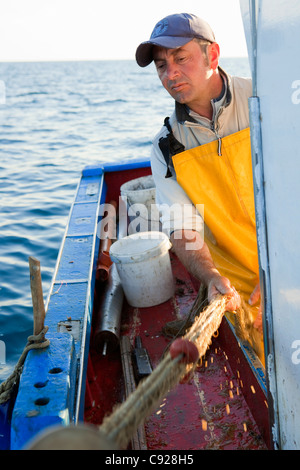 Fisherman reeling in nets on boat Stock Photo