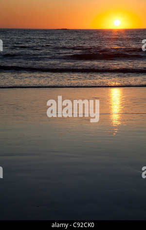 Sun setting over ocean on beach Stock Photo