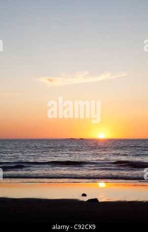 Sun setting over ocean on beach Stock Photo