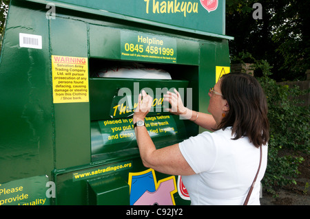 A woman puts a bag of clothing in a Salvation Army charity collection point for unwanted clothing & shoes. Stock Photo