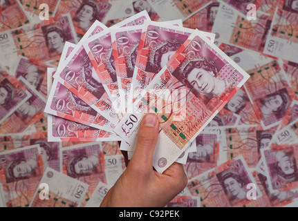 Hand full of new £50 fifty pound notes against background of 50 bank notes rich wealthy Stock Photo