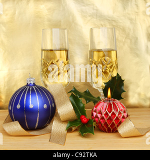 Christmas themed still life of champagne in glasses decorations and a burning decorative candle against a gold background Stock Photo