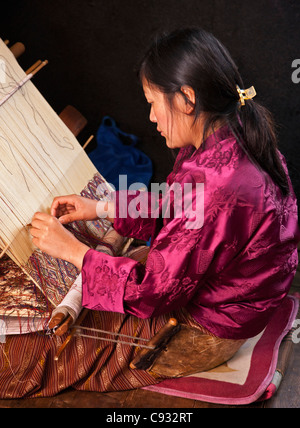 A woman weaves an intricate pattern in silk on her traditional wooden loom. Stock Photo