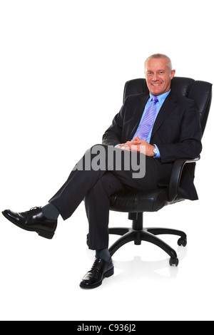 Photo of a mature businessman wearing a smart suit and tie, sat in a leather executive chair with his legs crossed Stock Photo