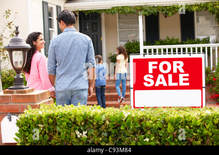 Hispanic family outside home with for sale sign Stock Photo