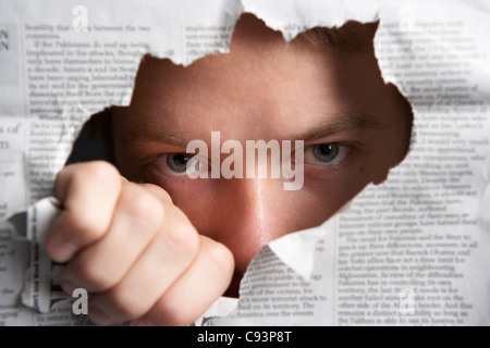 Man looking through hole in newspaper Stock Photo