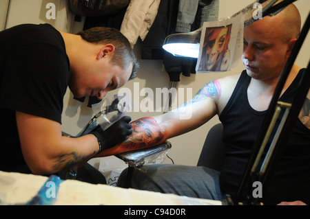 12.11.2011 Warsaw, Poland. Tattooist creates a tattoo on his client's forearm during the first day of tattoo, body painting and pierceing show - 'Body Art Convention' in Palace of Culture and Science in Warsaw. Stock Photo