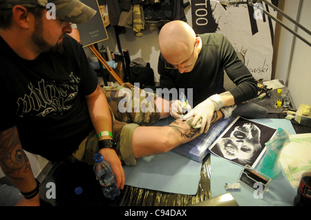 12.11.2011 Warsaw, Poland. Tattooist creates a tattoo on his client's leg during the first day of tattoo, body painting and pierceing show - 'Body Art Convention' in Palace of Culture and Science in Warsaw. Stock Photo