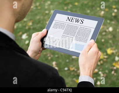 Businessman reading news on digital tablet at park. Stock Photo