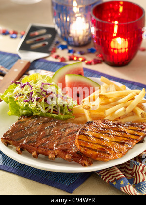 Barbecue pork ribs and chicken served with coleslaw, french fries and watermelon in a Fourth of July setting Stock Photo