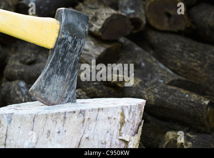 an ax on a wooden chopping block with a kiawe wood pile in background Stock Photo