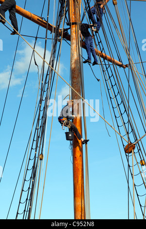 Girl with sanding machine - young sailors are sandpapering the mast and rig of 35m topsail schooner Lilla Dan in Copenhagen. Stock Photo