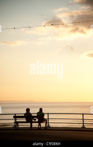 silhouette rear view of two men sitting on a bench at sundown, looking out to sea, aberystwyth wales uk Stock Photo