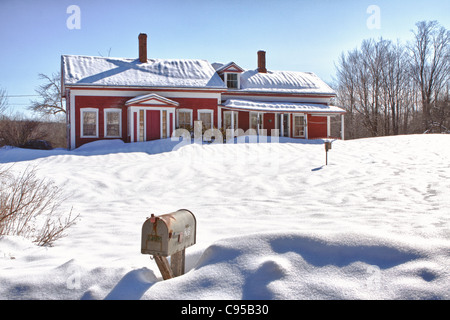 A mailbox in front of a red snow covered cape cod style house Stock Photo