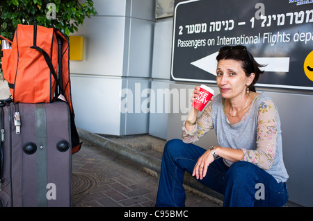 Woman drinking coffee while waiting with luggage at Terminal 1 at Ben-Gurion Int'l Airport. Tel-Aviv, Israel. 18/09/2011. Stock Photo