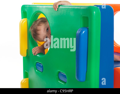 One and a half year old child looking out of a round window in a climber toy. Isolated on white background. Stock Photo