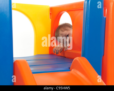 Tired one and a half year old child looking out of a round window in a climber toy after a good climbing workout Stock Photo