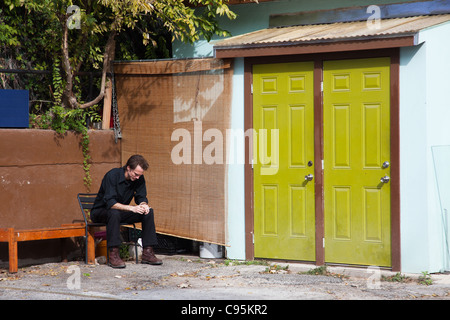 A sitting man looking down in a corner next to a colorful shed Stock Photo