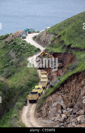 A digger fills waiting trucks with earth in order to widen a road above Lake Toba. Pangururan, Lake Toba, Sumatra, Indonesia Stock Photo