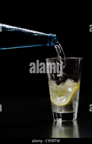 Mineral water is poured into a glass with ice and lemon Stock Photo