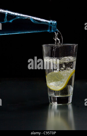 Mineral water is poured into a glass with ice and lemon Stock Photo