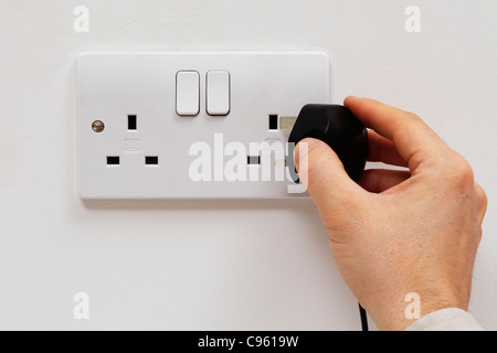 Plug being inserted into wall Stock Photo