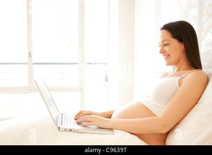 Pregnant woman using a laptop in bed. Stock Photo